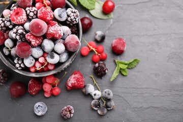Mix of ripe frozen berries, mint leaves and bowl on dark textured table, flat lay. Space for text