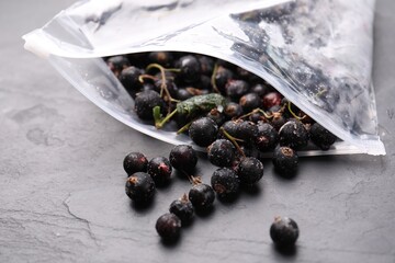 Ripe frozen black currants and open plastic bag on grey textured table, closeup