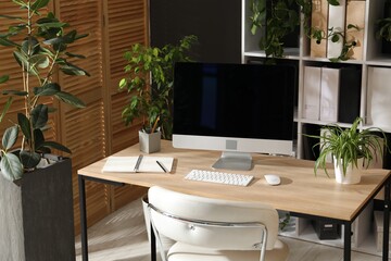 Stylish workplace with modern computer, stationery and floral decor in office. Biophilic interior design