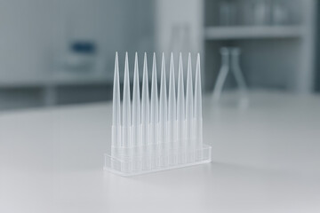 Transparent pipette tips neatly arranged in a plastic rack on a laboratory table with blurred lab equipment in the background.