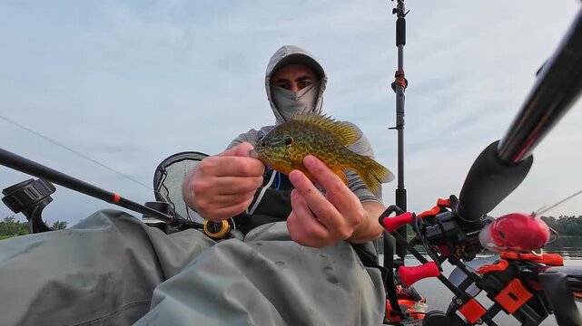 Angler in kayak catch and release nice panfish bluegill with hook and worm lure in its mouth, summer activity, kayaking and fishing outdoors. Kayak fisherman display his catch and release.
