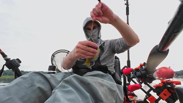 Angler in kayak catch and release nice panfish bluegill with hook and worm lure in its mouth, summer activity, kayaking and fishing outdoors. Kayak fisherman display his catch and release.