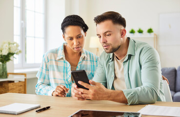 Female and male students gathering together, focused in smartphone, studying and trying to find necessary information in internet, sitting at desk with notepads, surfing social networks