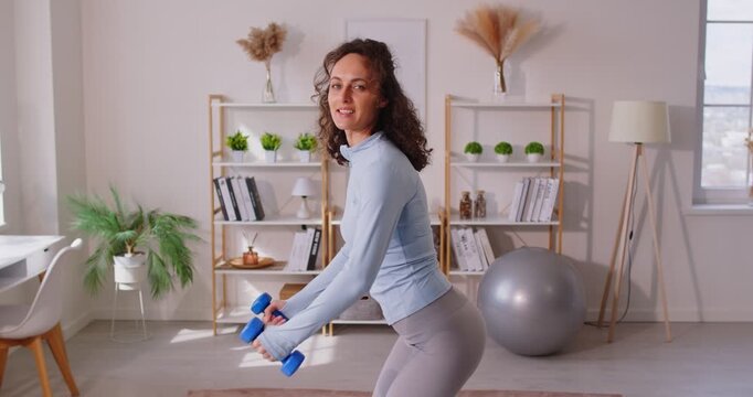 Sporty motivated woman lifting dummbells, doing workout while staying at home, posing in living room, motivating you to do regular exercise and keeping fit. Healthy lifestyle concept