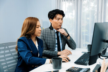 Business Asian coworkers analyzing marketing report project on two screen computer comparing value stock exchange database online report at modern office. Analyzing value investment company. Infobahn.