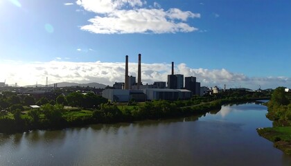 Obraz premium Industrial complex alongside a river on a sunny day.