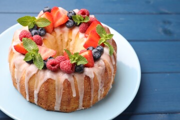 Delicious bundt cake with berries, glaze and mint on blue wooden table, closeup