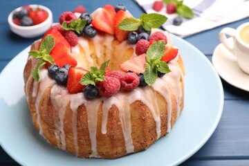 Delicious bundt cake with berries, glaze and mint on blue wooden table, closeup