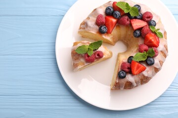 Pieces of delicious bundt cake with berries, glaze and mint on light blue wooden table, top view. Space for text