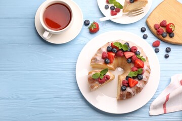 Pieces of delicious bundt cake with berries, glaze and mint served on light blue wooden table, flat lay