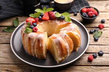 Pieces of delicious bundt cake with berries, glaze and mint on wooden table, closeup