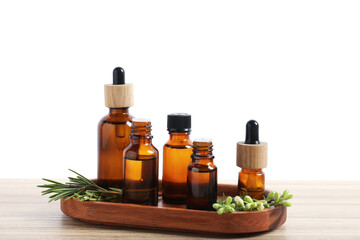 Bottles of essential oils and different herbs on wooden table against white background