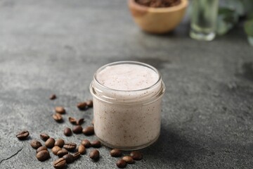 Natural body scrub in glass jar and coffee beans on grey table, closeup
