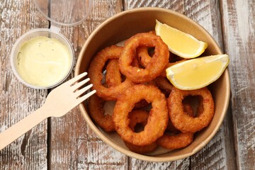 Fried squid rings, lemon and sauce on wooden table, flat lay