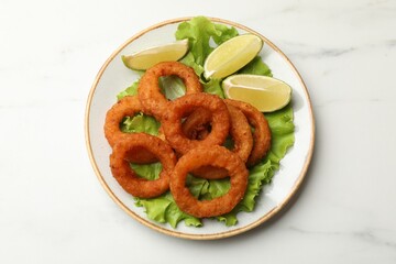 Fried squid rings, lime and lettuce on white marble table, top view