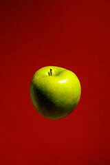 Whole green apple levitates on red background, symbol of wellness, organic farming, vitamins, fitness training, and nutritious lifestyle