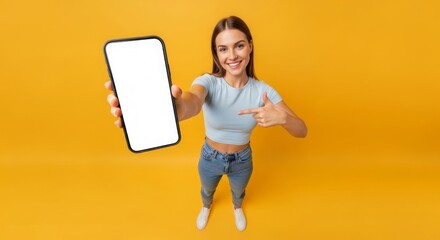 Smiling woman in casual attire showcasing a blank smartphone screen with an orange backdrop, perfect for app promotion or mobile content