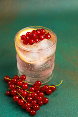Refreshing lemonade cocktail garnished with red currants and lemon slice on a teal background