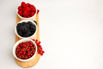 Colorful variety of fresh berries arranged in bowls on a wooden platter on a neutral background