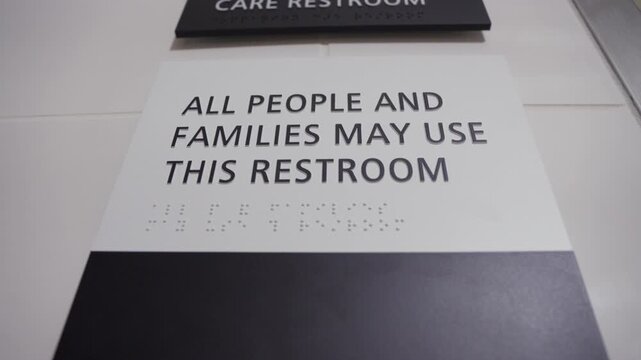 Close-up of restroom signage, captured from a bottom-up angle. All people and families may use this restroom is in focus, above it is a companion care restroom icon.