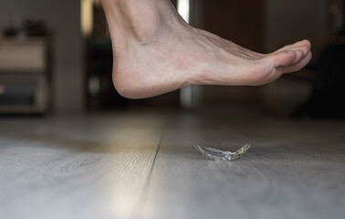 A man's bare feet is a second away from stepping on a broken piece of sharp glass at his home wooden floor. Accident at home concept.