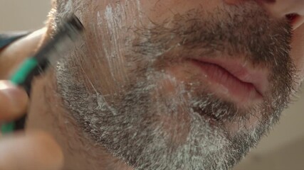 Close up of a man shaving his beard with a green and black razor