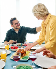 Happy multi-generation family gathering around dining table and having fun during a lunch or dinner on holiday or weekend, senior couple, grandparents, grandmother and grandfather eating