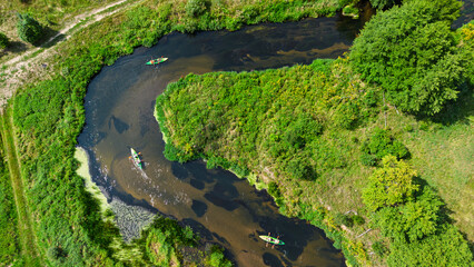 Aerial drone view of colorful kayaks floating along the winding Liswarta River, river surrounded by lush green meadows and summer nature landscape. Kayaking on river in Poland. Kayaks on a river