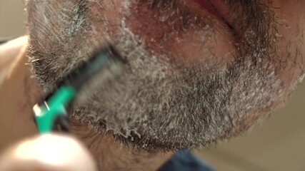 Close up of a man shaving his beard with a green and black razor