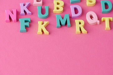 Brightly colored letters are scattered across a pink surface, creating a playful and vibrant layout.