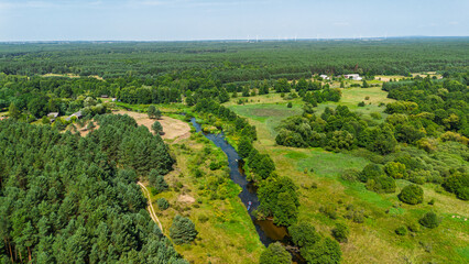 Aerial drone view of colorful kayaks floating along the winding Liswarta River, river surrounded by lush green meadows and summer nature landscape. Kayaking on river in Poland. Kayaks on a river