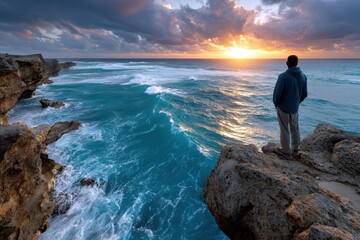 Person enjoys a sunrise by the ocean on a rocky cliff, capturing the beauty of nature