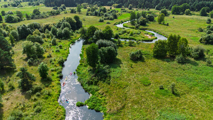 Aerial drone view of colorful kayaks floating along the winding Liswarta River, river surrounded by lush green meadows and summer nature landscape. Kayaking on river in Poland. Kayaks on a river