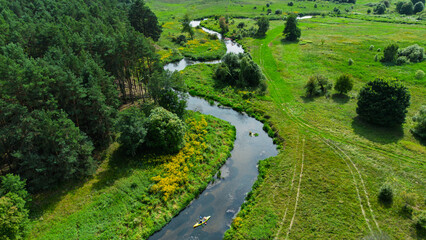 Aerial drone view of colorful kayaks floating along the winding Liswarta River, river surrounded by lush green meadows and summer nature landscape. Kayaking on river in Poland. Kayaks on a river