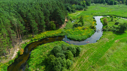 Aerial drone view of colorful kayaks floating along the winding Liswarta River, river surrounded by lush green meadows and summer nature landscape. Kayaking on river in Poland. Kayaks on a river
