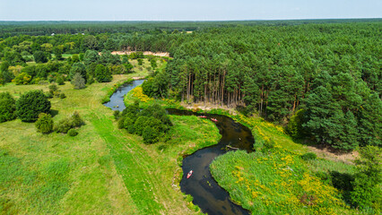 Aerial drone view of colorful kayaks floating along the winding Liswarta River, river surrounded by lush green meadows and summer nature landscape. Kayaking on river in Poland. Kayaks on a river