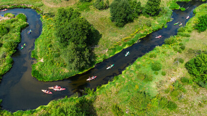 Aerial drone view of colorful kayaks floating along the winding Liswarta River, river surrounded by lush green meadows and summer nature landscape. Kayaking on river in Poland. Kayaks on a river