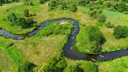 Aerial drone view of colorful kayaks floating along the winding Liswarta River, river surrounded by lush green meadows and summer nature landscape. Kayaking on river in Poland. Kayaks on a river