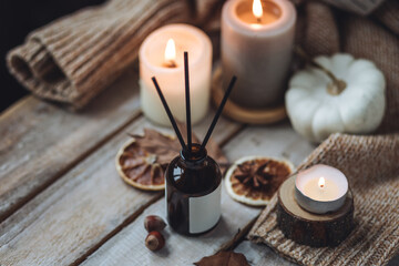 Concept of house decor, apartment seasonal fragrance. Thanksgiving. Autumn mood, cozy fall home atmosphere. Aroma diffuser, pumpkins, knitted warm sweaters, burning candles, dry leaves on wooden table