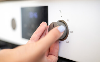 A close-up of a hand adjusting the temperature dial on an oven, showcasing modern kitchen appliances in a bright environment.