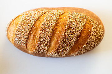 A freshly baked loaf of bread topped with sesame seeds, showcasing a golden-brown crust and distinct scoring.