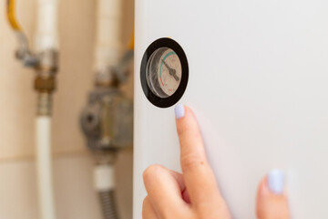 A close-up of a person checking the pressure gauge of a boiler, showcasing a hand with light purple nails.