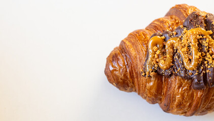 A delicious croissant topped with rich chocolate and caramel drizzle, sprinkled with crushed nuts for texture.