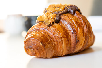 A delectable close-up of a golden brown croissant topped with chocolate and caramel, showcasing a crispy texture.
