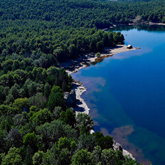 Obraz premium Stunning aerial view of a crystal-clear blue lake surrounded by a vibrant green forest.
