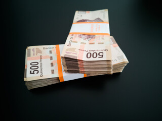 Un fajo de billetes de 500 pesos mexicanos sobre un fondo negro.
A wad of 500 Mexican peso bills on a black background.