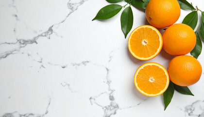 A top-down view of fresh oranges and green leaves on a white marble background.