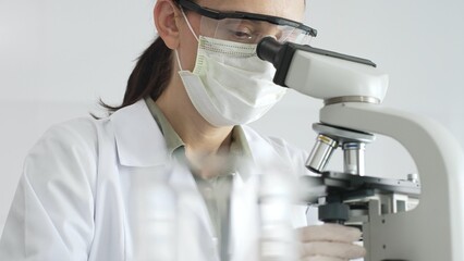 Female scientist examining microscope slide, wearing white protective gear while conducting medical research in laboratory environment. Medicine, health care and science concept
