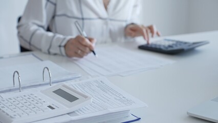 White calculator is on financial documents on the office desk, with an accountant taking notes, emphasizing accounting, finance, and tax preparation, close up. Audit and taxes concept
