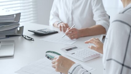Two accountants collaborating on financial analysis, using a magnifying glass, calculator, and laptop to ensure data accuracy. Audit and taxes in business